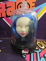 Front view of Monster High doll head with blue hair inside clear dome on black base