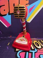 Front view of red, white and gold North Pole Communicator toy microphone on stand