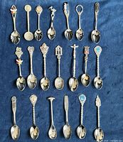 Twenty souvenir spoons arranged in four rows on blue surface