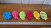 Six crocheted water balloons lined up beside ruler showing size
