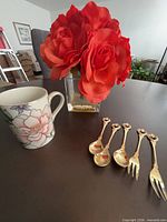 Group view of mug, rose arrangement, and gold-tone utensils on table