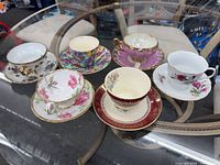 Six assorted bone china teacup and saucer sets arranged on glass table