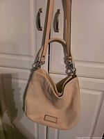 Full view of handbag hanging to show overall form, color, straps, hardware