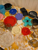 Overview of assorted plastic plates, bowls, cups, utensils, bakeware, amber goblets and pressed glass pieces