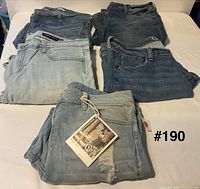 Five folded pairs of women’s jeans showing assorted washes, one with hang-tag