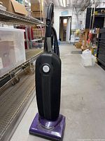 Full view of Riccar SupraLite upright vacuum standing on floor, showing purple base, black bag, handle and power cord
