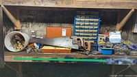 Full view of bench showing hand saws, metal drawer organizer, orange case, white bucket of knobs, blue tray of hardware