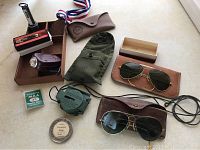 Various vintage military collectibles including compass, sunglasses, badge, matchbox, metal token, flashlight, and knife on beige surface