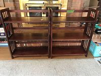 Front view showing two matching folding wooden shelves side by side with three shelves each in front of a fireplace.