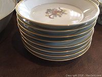 Stack of saucers and plates showing wreath and ribbon motif with gold rims