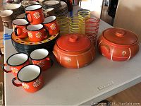 Metal plates, metal cups, glasses, and ceramic crocks displayed on table