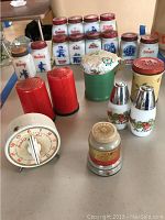 Angle view showing arrangement of 12 white glass spice containers with red metal lids and a vintage timer and shakers in front.