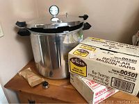Presto pressure cooker canner next to boxed Kerr regular Mason jars and jelly jars on wooden table.