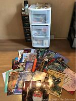 Photo showing a collection of decorative painting books laid out on the floor in front of two storage units containing supplies.