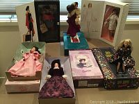 Photo showing six Barbie dolls in original boxes with varied themed outfits, including Victorian-style and modern fashion.