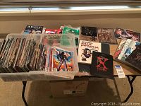 Bin filled with numerous colorful Japanese comic books, mostly manga, neatly organized and displayed on a table with additional items beside them.