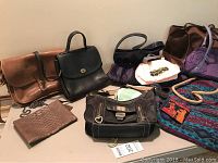Full view of multiple purses including vintage Coach leather bag, black purse, newer Coach bag with chain handle, and colorful totes