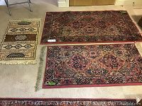 Three rugs displayed on carpeted floor: a large Karastan rug, a smaller Karastan rug, and a smaller geometric pattern rug.