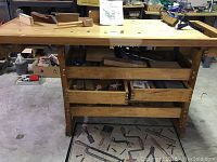 Front view of workbench showing laminated wooden top with bench dog holes, vises, drawers and shelves