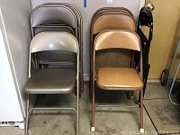 Overall view of gray metal folding chairs and Samsonite folding chairs with light brown cushioned seats stacked in pairs.