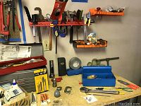 Wide shot of three wall-mounted racks and workbench surface with various hand tools including clamps, files, wires, and small hardware items.