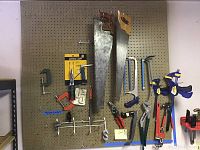 Full view of peg board with tools hung in organized manner including saws, clamps, pliers, and hooks