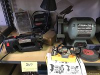 View of a Delta 6-inch bench grinder with grinding wheels, Rotozip spiral saw, user manual, box, and safety glasses on a work surface.