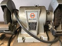 Black & Decker 5-inch bench grinder with grinding wheel and wire brush wheel visible, power cord attached.