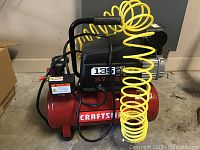 Side view showing red horizontal tank labeled 'Craftsman' with black motor housing and yellow coiled air hose attached.