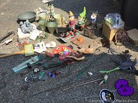 Wide view photo showing all yard decor items spread on pavement including pots, statues, hanging chimes, garden poles with ornaments, and boxed watering can.