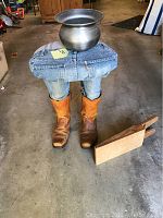 Front view of the bench with denim jeans, cowboy boots, metal spittoon on top, and boot puller on the floor
