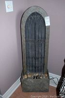 Full front view of the electric indoor fountain showing gothic arched panel and base with decorative stones and power cord.