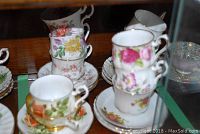 Eleven assorted floral tea cups stacked and displayed with matching saucers, showing variety in design and gold trim wear.