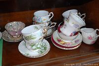 Six assorted bone china cups and matching saucers with floral patterns on wooden shelf