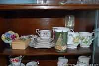 Shelved display of assorted china items including mugs, cups, saucers and decorative bowl