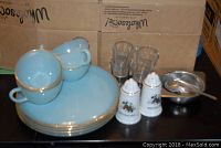 Overview of the set showing four blue cups stacked on saucers, clear liquor glasses, metal sugar bowl with spoon, and souvenir salt and pepper shakers.