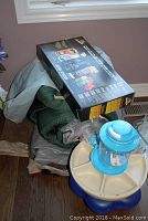 Sleeping bag with air mattress pump in clear bag and partially visible box and tray on soft surface near window