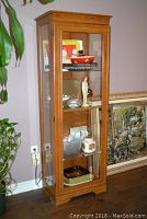 Full view of wooden display cabinet showing front glass door with items inside and sides also made of glass.