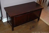 Angled side view of wooden chest bench showing top surface and front panel with wear marks.