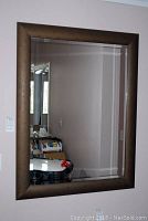 Full view of the rectangular wall mirror showing beveled glass and a brown wood-look frame hung on a wall.