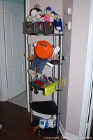 Full view of black corner shelving unit with four shelves loaded with stuffed toys, basket, and a pumpkin-themed decoration.