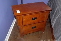 Front-side view of wooden night stand showing drawer fronts and metal pulls with visible scratches on the top and front surfaces.