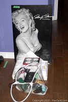 Photo showing framed Marilyn Monroe poster with golf ball and trivet set in box and luxury hotel robe on floor
