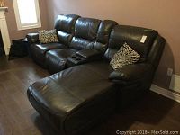 Angle showing full sofa with chaise extension on the right, dark brown faux leather upholstery and two zebra print pillows.