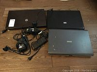 Three closed laptops (HP ProBook 4720s, HP C6830s, Toshiba Satellite P100) laid on floor with power adapters and cords.