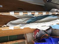 Side view of rolled canvas hammock featuring wooden spreader bars and white braided rope ends laying on a wooden surface.