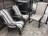 Two plastic patio chairs with white and black striped cushions and one metal framed patio chair with beige mesh seating on patio.