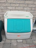 Front view of white plastic toy box showing teal flip-down lid and Step 2 logo sticker on bottom center.