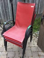 Four stackable red patio chairs with black metal frames, showing fading on fabric surfaces.