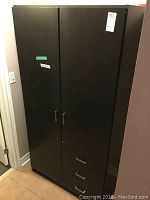 Front view of the black laminate armoire with two doors and three drawers at the bottom.
